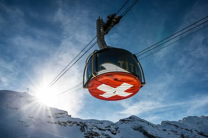 Titlis cable car with a Swiss flag design hanging above snowy mountains