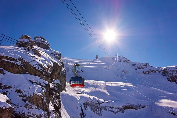 A cable car moving up the mountain under a bright sunny sky