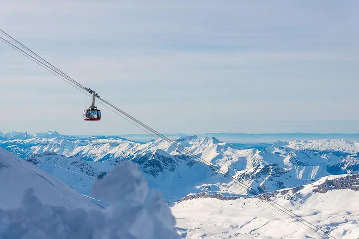 A cable car ascending over a snowy alpine landscape with mountains beyond