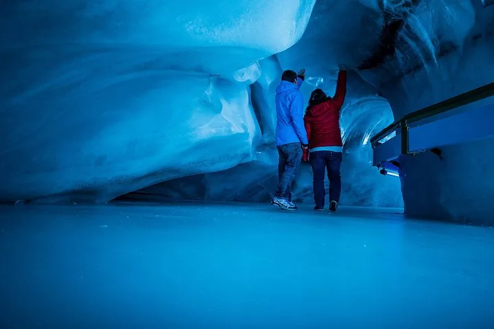 Two people exploring the glowing blue ice cave at Mount Titlis