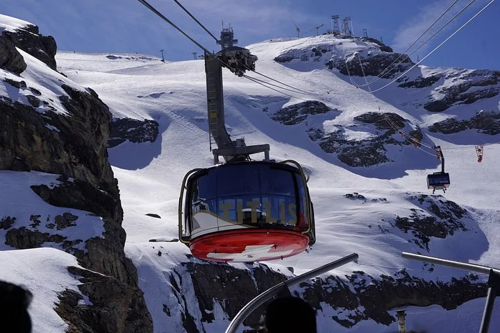 A red Titlis Rotair cable car traveling against a snowy mountain backdrop